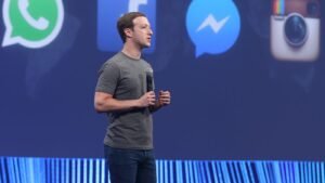 Mark Zuckerberg, Meta CEO, in grey shirt, presenting, holding a microphone in front of a backdrop of Facebook, Whatsapp, Instagram and Messenger logos. Whatsapp Monetization
