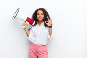 Beautiful, light-skinned, and smiling African woman, holding a megaphone on her right hand, while making the OK sign with her left hand, posing for an online business